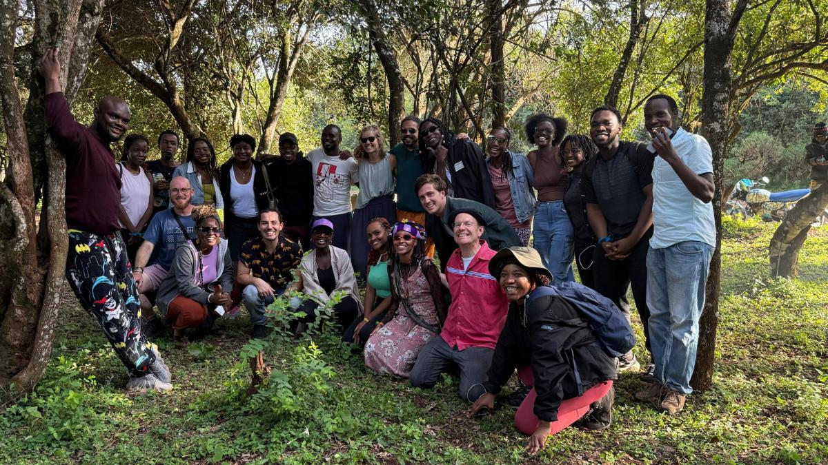 A large group of smiling volunteers gathered outdoors in a forest after completing the River Kandisi cleanup. They are standing and crouching in a semi-circle, surrounded by trees and greenery